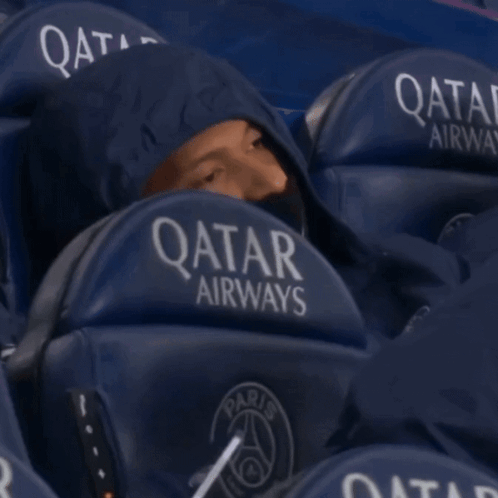 a man wearing a hoodie sits in a qatar airways stadium seat