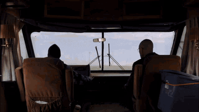 two men are sitting in a bus looking out the window with a blue cooler in front of them