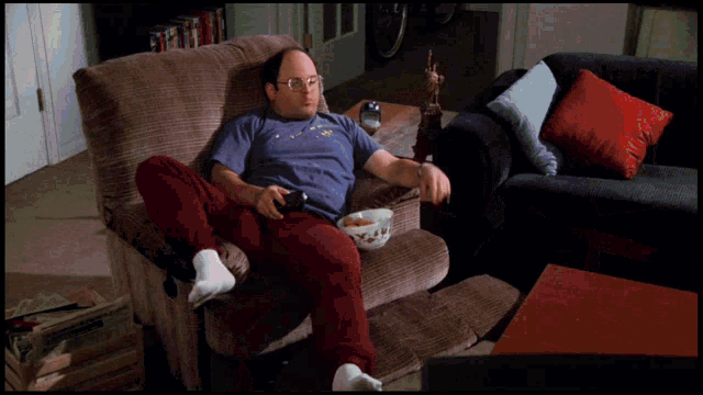 George Costanza relaxes in an armchair beside junk food.