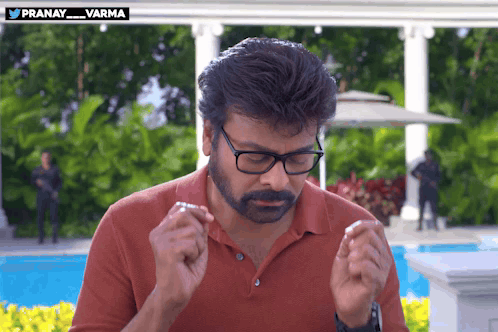 A man in glasses makes an apologetic hand gesture outdoors.
