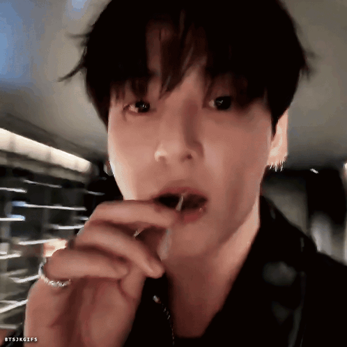 A man holds a lollipop at his mouth while looking into the camera.