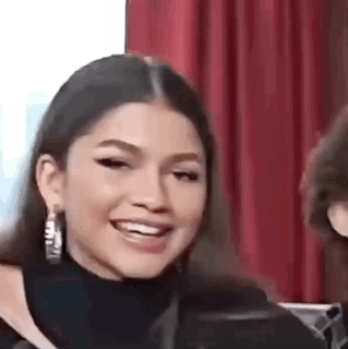 Zendaya smiles and looks toward someone beside her.