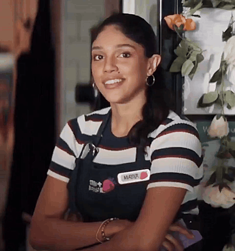 a woman in a striped shirt and apron is smiling while standing in front of a door .