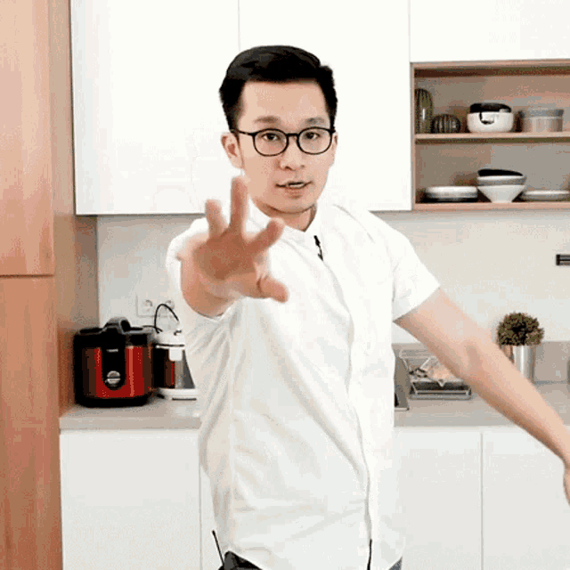 a man wearing glasses and a white shirt is standing in a kitchen with his arm outstretched