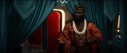 a man in a red robe is standing in front of a blue curtain with the words what the hell written on it