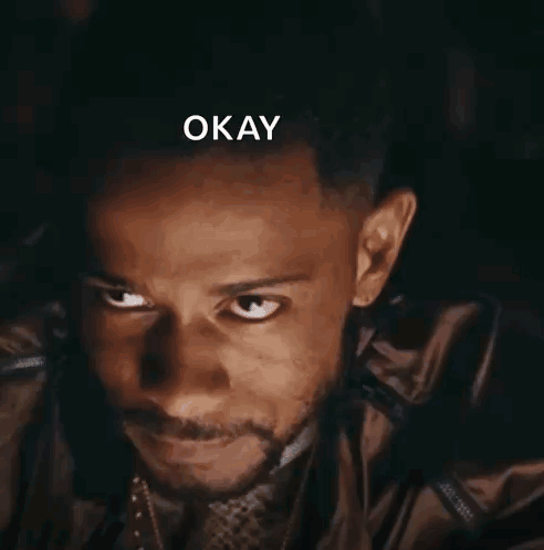 A man gives a dark, intense smile beneath the caption “OKAY.”