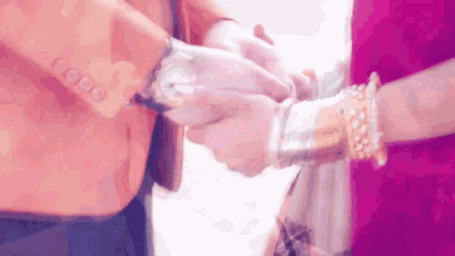 a man and woman are holding hands and the woman is wearing gold bracelets .