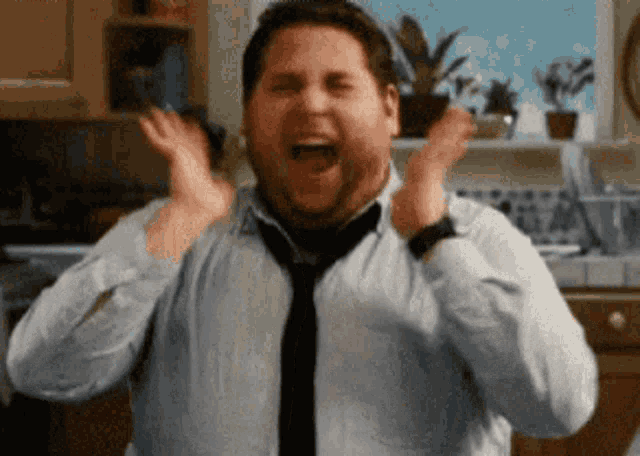 A man claps excitedly with a delighted open-mouthed expression.