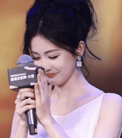 Bai Lu smiles awkwardly while holding a microphone and a card.