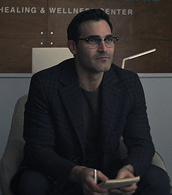 a man wearing glasses is sitting in front of a sign that says healing and wellness center