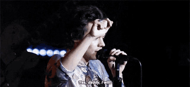 a man is singing into a microphone on a stage and saying yes , daddy , i will .