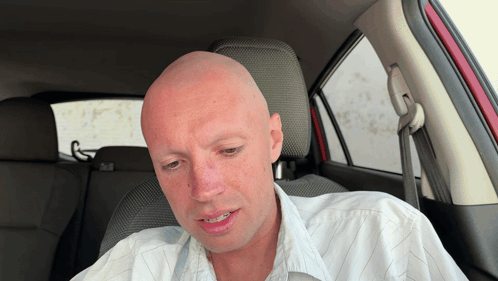 a bald man is sitting in the back seat of a car with his eyes closed