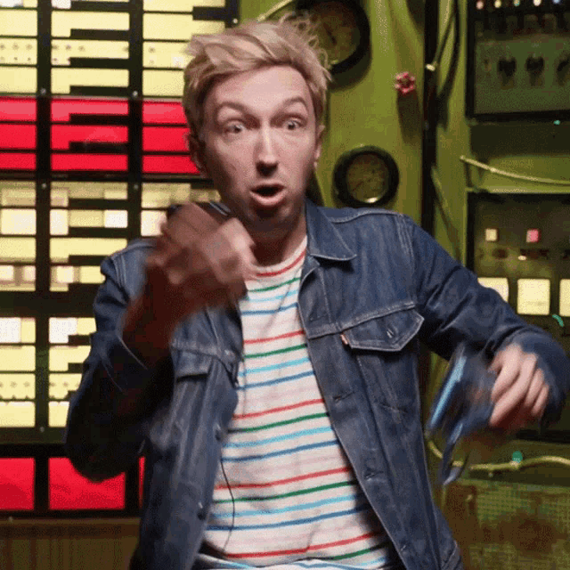 a man wearing a striped shirt and a denim jacket is standing in front of a green wall
