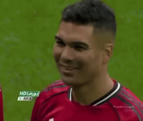 a man wearing a red manchester united jersey is smiling on a soccer field .