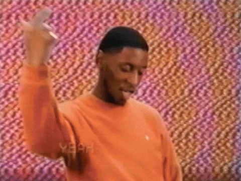 A man in an orange shirt dances happily against a colorful backdrop.