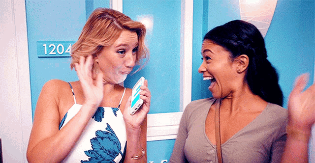Two women from Jane the Virgin grin at one another while raising their hands.