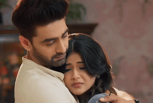 A couple share a comforting embrace in a warm indoor scene.
