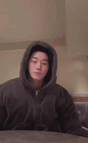 a man wearing a hoodie is sitting at a table with his eyes closed .