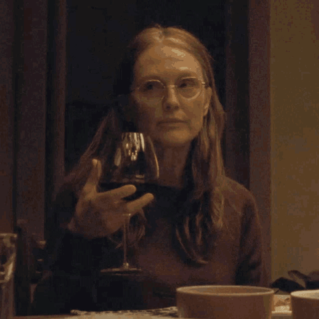a woman wearing glasses is holding a glass of red wine