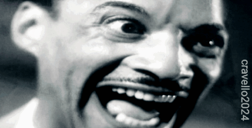 A black-and-white close-up shows a man grinning with intense wide eyes.