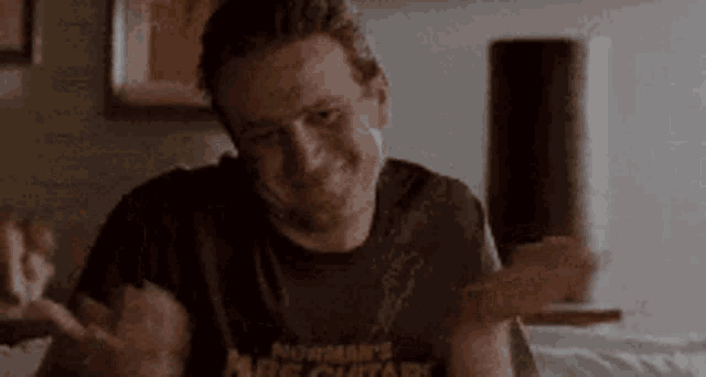 A man leans forward indoors with both palms raised in a shrug.