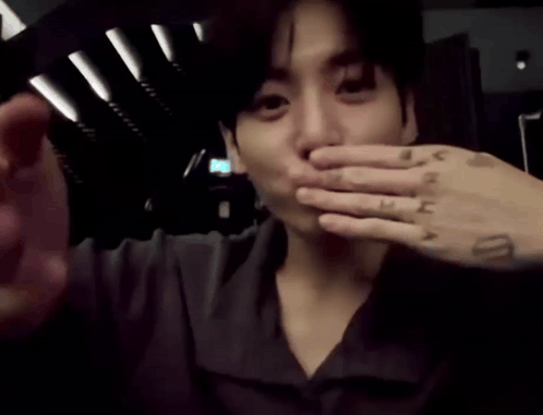 Jungkook raises a hand to his mouth as if blowing a kiss.
