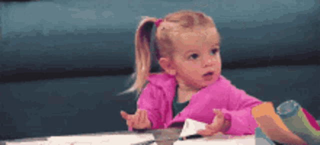 A little girl at a table gives a firm, playful no gesture.