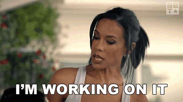 a woman says " i 'm working on it " while wearing a white tank top