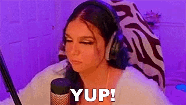 a woman wearing headphones is sitting in front of a microphone and saying yup !