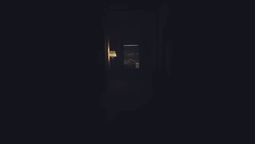 a dark room with a lamp and a person sitting in a chair