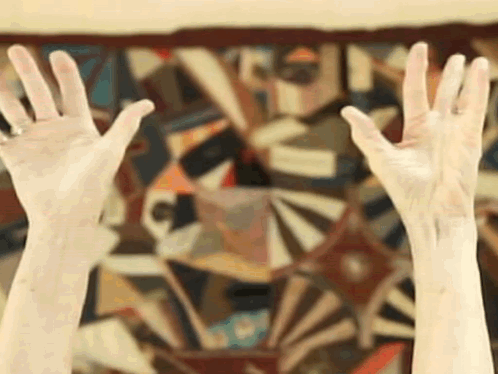 a person 's hands are up in front of a colorful painting
