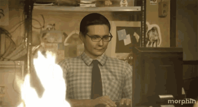 a man in a plaid shirt and tie is typing on a keyboard in front of a monitor that says morphin on it