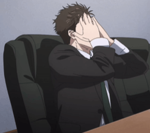 An anime man in a dark suit covers his face while seated on a couch.