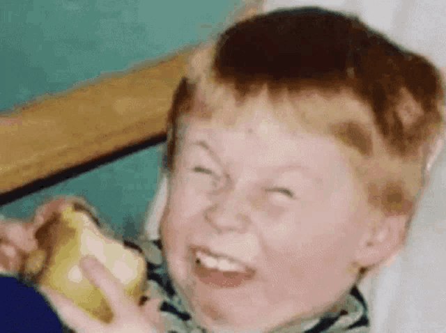 A child grins with eyes squeezed shut while holding food.