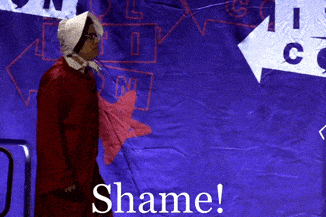 a woman in a red dress is standing in front of a sign that says " shame "