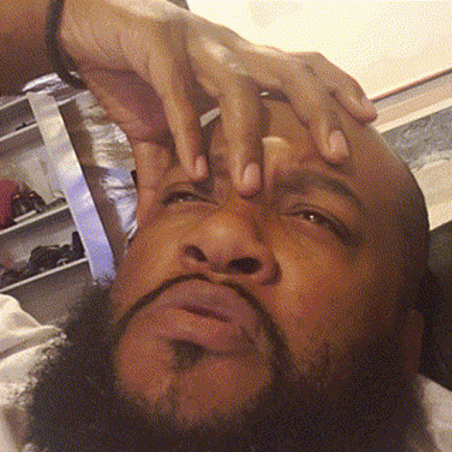 A bearded man presses a hand to his forehead while pondering.
