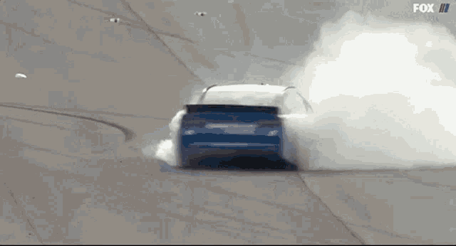 a blue car is drifting on a track with smoke coming out of it