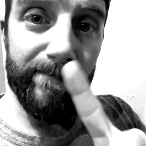 A bearded man shakes a finger at the camera in black and white.
