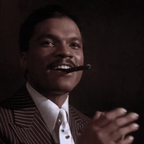 A man in a striped suit claps with a cigar in his mouth.