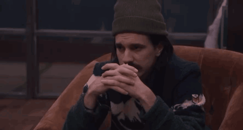 a man wearing a beanie and a sweater has his hands on his head