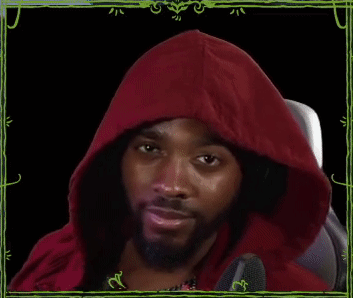 A man in a red hood gives a subtle wink while seated at a microphone.