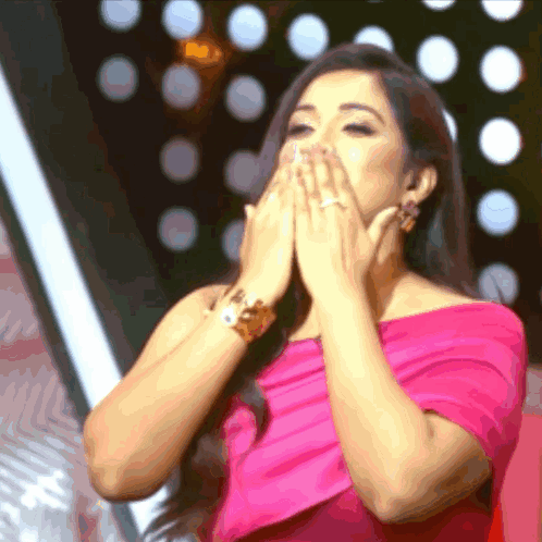 Woman in bright pink blows kisses with her hands near her face.