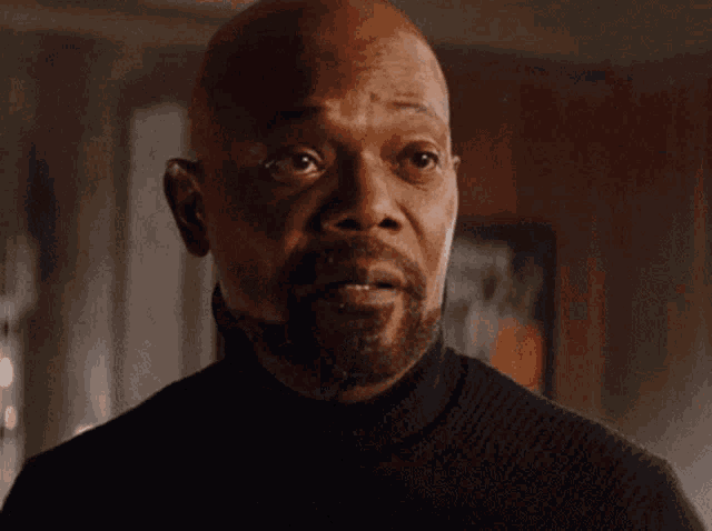 A bald man looks forward skeptically with a restrained reaction.