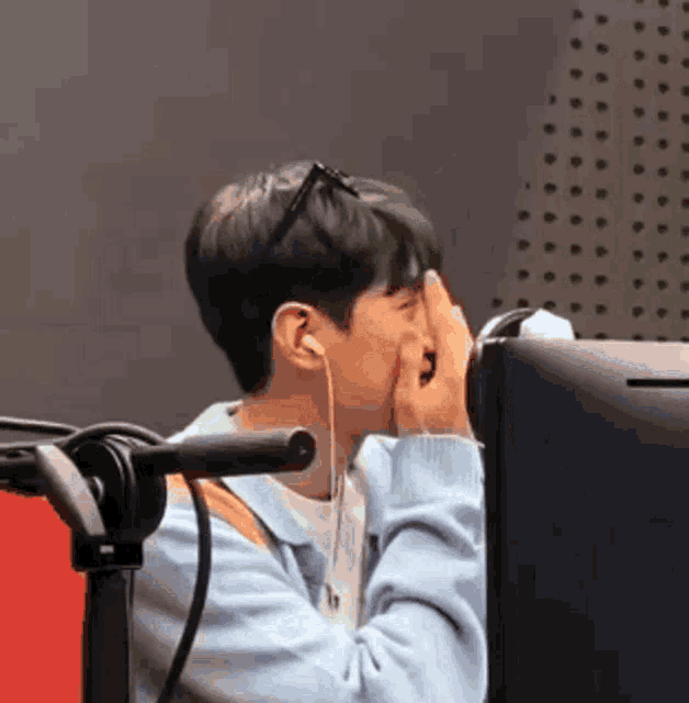 a man wearing headphones is sitting in front of a microphone and covering his face .