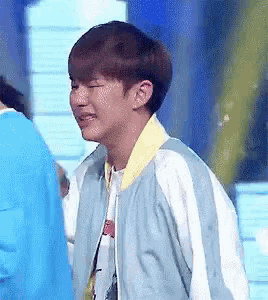 a young man wearing a blue jacket and a yellow collar is standing in front of a blue wall .