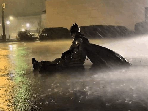 Batman sits alone in heavy rain at night.