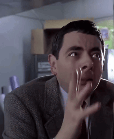Mr. Bean raises a hand to his face in alarm.
