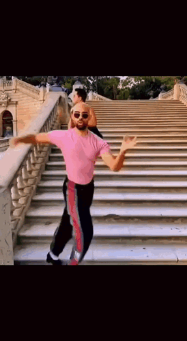 a man in a pink shirt is dancing on stairs