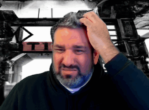 A bearded man scratches his head with a puzzled expression.