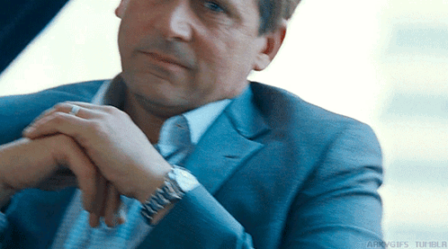 a man in a suit and tie with his hands folded and a watch on his wrist